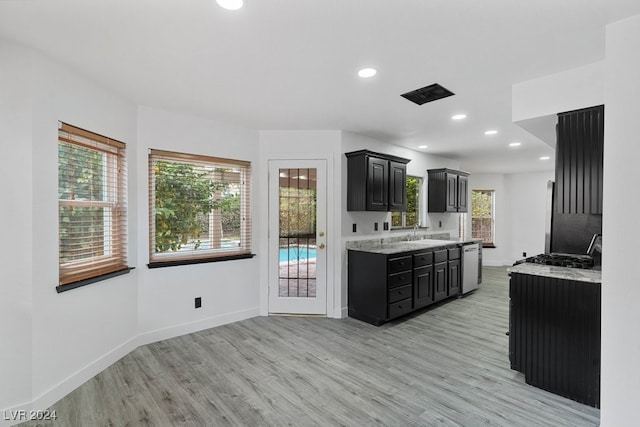 kitchen with stainless steel dishwasher, light stone countertops, light wood-type flooring, and sink