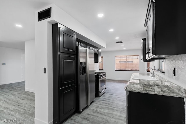 kitchen featuring light stone countertops, appliances with stainless steel finishes, light wood-type flooring, and sink