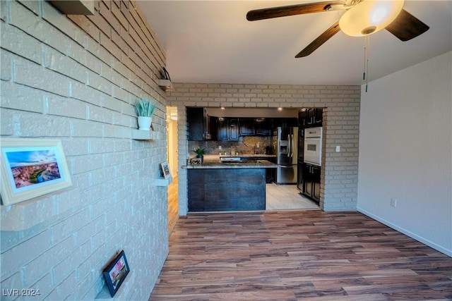 kitchen with dark brown cabinetry, stainless steel refrigerator with ice dispenser, oven, wood-type flooring, and decorative backsplash