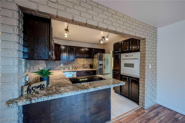 kitchen with dark brown cabinetry, kitchen peninsula, decorative backsplash, appliances with stainless steel finishes, and light wood-type flooring