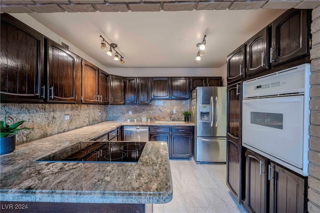 kitchen featuring appliances with stainless steel finishes, backsplash, light stone counters, dark brown cabinets, and sink