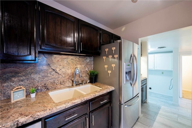 kitchen featuring decorative backsplash, stainless steel fridge, light stone counters, dark brown cabinetry, and sink