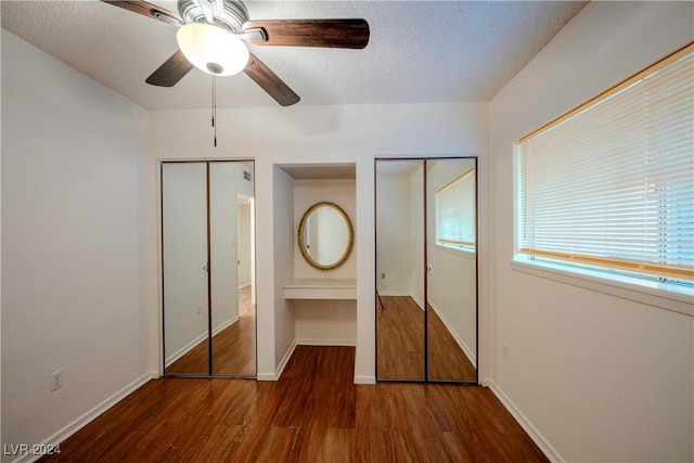 unfurnished bedroom featuring a textured ceiling, ceiling fan, dark wood-type flooring, and two closets