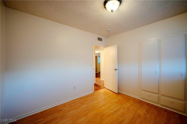 unfurnished bedroom featuring a textured ceiling, light hardwood / wood-style flooring, and a closet