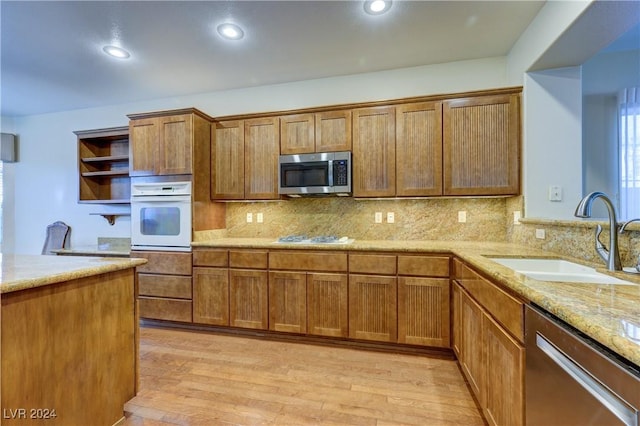 kitchen with sink, tasteful backsplash, light stone counters, appliances with stainless steel finishes, and light wood-type flooring