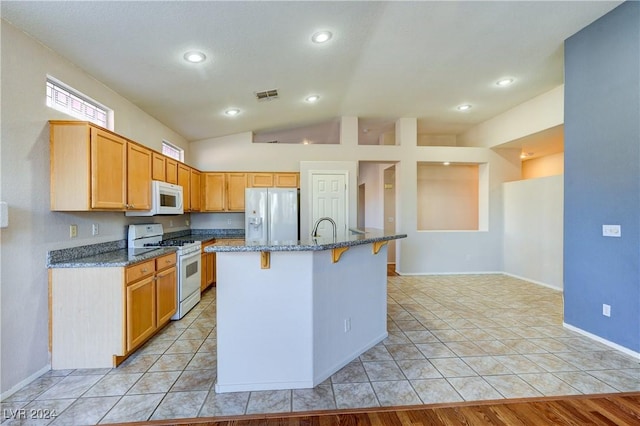 kitchen with lofted ceiling, white appliances, a center island with sink, dark stone countertops, and light wood-type flooring