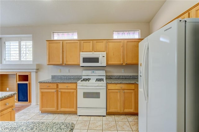 kitchen with stone counters, light tile patterned floors, white appliances, and a wealth of natural light