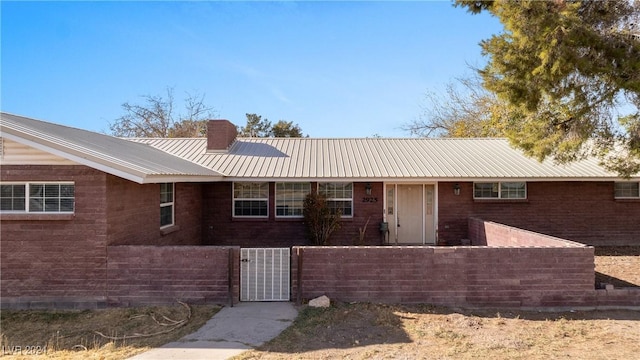 ranch-style home featuring brick siding, a fenced front yard, metal roof, a chimney, and a gate