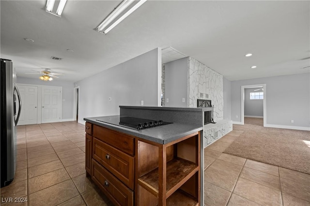 kitchen with ceiling fan, stainless steel fridge, black electric cooktop, a fireplace, and a kitchen island