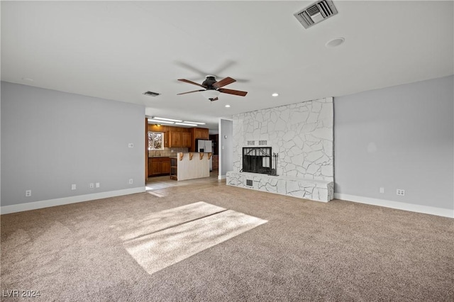 unfurnished living room featuring ceiling fan, a stone fireplace, and light carpet