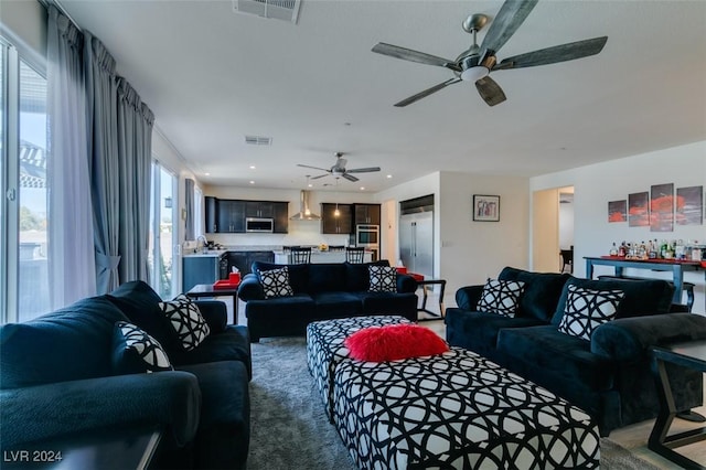 living room featuring carpet, ceiling fan, a healthy amount of sunlight, and bar area