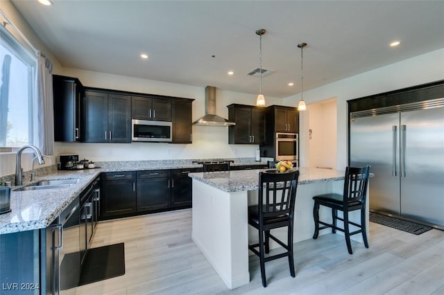 kitchen featuring a center island, wall chimney exhaust hood, hanging light fixtures, stainless steel appliances, and sink