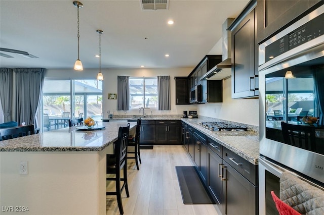 kitchen featuring light stone countertops, appliances with stainless steel finishes, a kitchen bar, light hardwood / wood-style floors, and a kitchen island