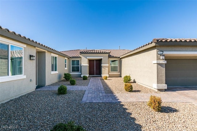 view of front facade featuring a garage, decorative driveway, a tile roof, and stucco siding