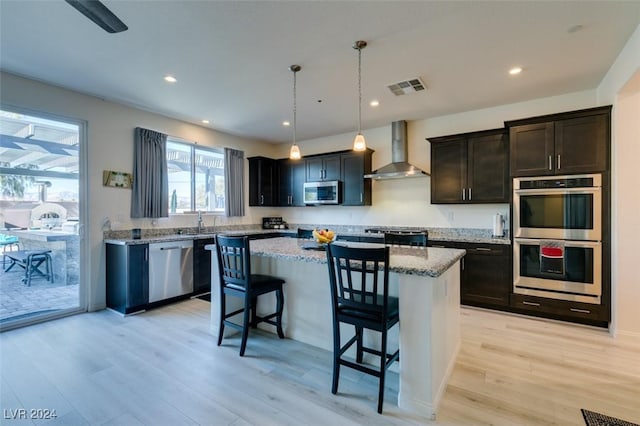 kitchen with wall chimney range hood, stainless steel appliances, and light hardwood / wood-style flooring