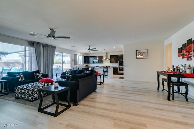 living room featuring bar area, light wood-type flooring, and ceiling fan