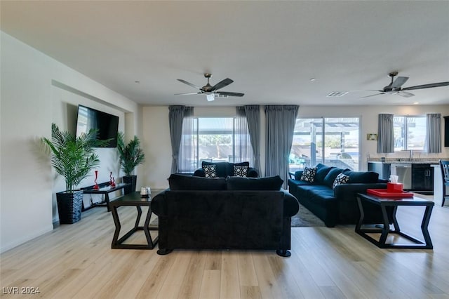 living area with a wealth of natural light, light wood-type flooring, and a ceiling fan