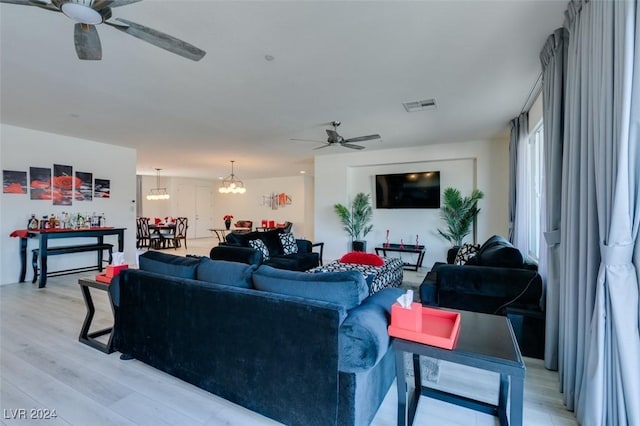 living room with light wood-style flooring, visible vents, and ceiling fan with notable chandelier