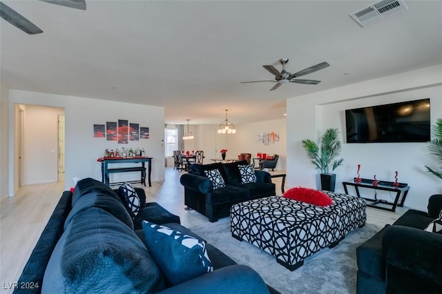 living area with ceiling fan with notable chandelier, visible vents, and wood finished floors