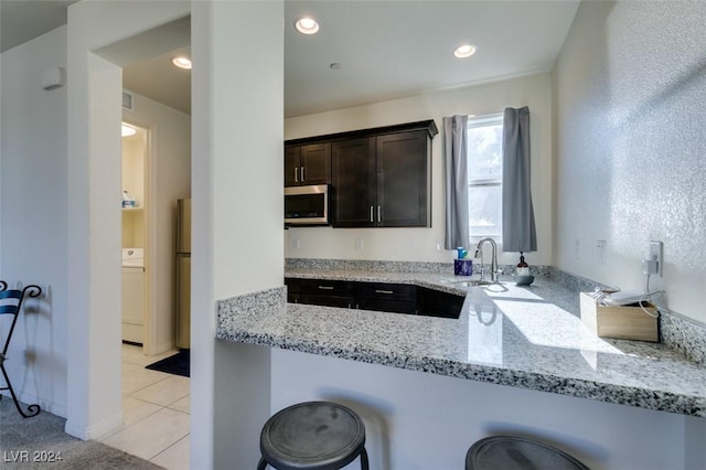 kitchen featuring a breakfast bar area, stainless steel appliances, washer / clothes dryer, dark brown cabinetry, and light stone countertops