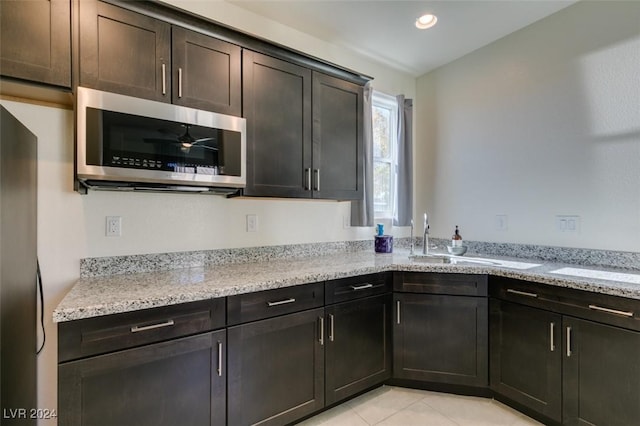 kitchen with light stone countertops, light tile patterned floors, stainless steel microwave, and a sink