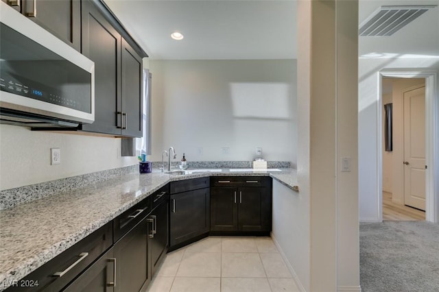 kitchen with light tile patterned floors, dark brown cabinetry, light stone counters, and sink