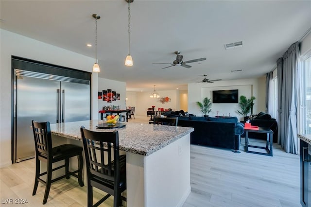 kitchen with light stone counters, built in fridge, visible vents, light wood-style floors, and a center island