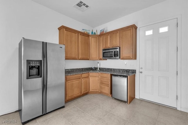 kitchen with dark stone countertops, sink, light tile patterned floors, and stainless steel appliances