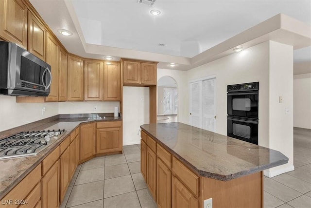 kitchen featuring dark stone counters, stainless steel appliances, a raised ceiling, a kitchen island, and light tile patterned flooring