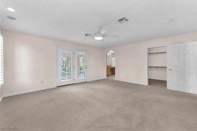 unfurnished bedroom with light carpet, access to outside, a walk in closet, ceiling fan, and a closet