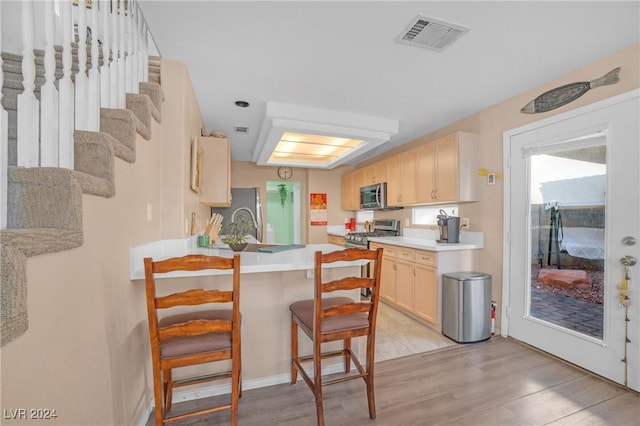 kitchen with light brown cabinets, a kitchen breakfast bar, light wood-type flooring, kitchen peninsula, and stainless steel appliances