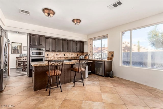 kitchen with decorative backsplash, appliances with stainless steel finishes, light stone countertops, a kitchen island, and a breakfast bar area