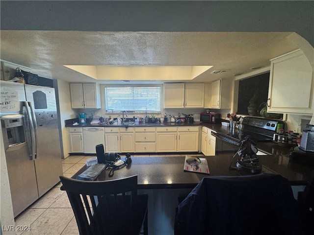 kitchen with sink, a textured ceiling, a tray ceiling, light tile patterned floors, and black appliances