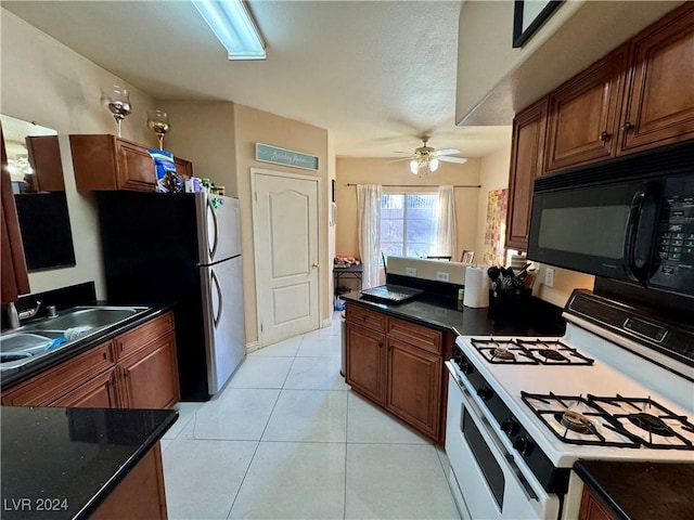 kitchen featuring sink, ceiling fan, light tile patterned floors, white gas stove, and stainless steel refrigerator