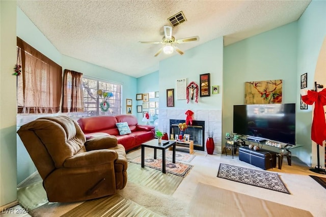 living room featuring light carpet, a tile fireplace, vaulted ceiling, ceiling fan, and a textured ceiling