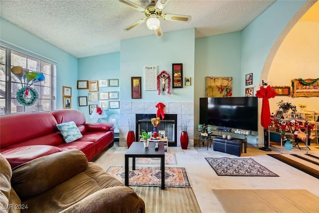 living room with carpet flooring, a textured ceiling, ceiling fan, a tile fireplace, and lofted ceiling