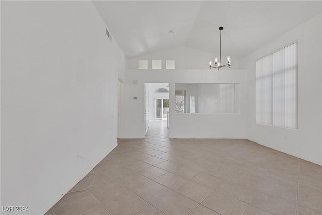 tiled spare room featuring a healthy amount of sunlight, lofted ceiling, and a chandelier