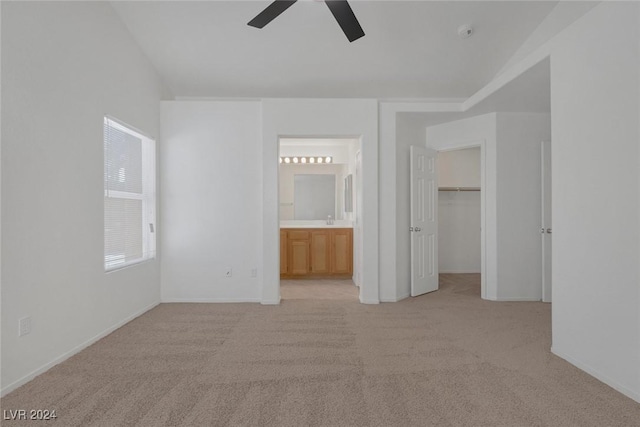 unfurnished bedroom featuring light carpet, ceiling fan, a spacious closet, connected bathroom, and a closet