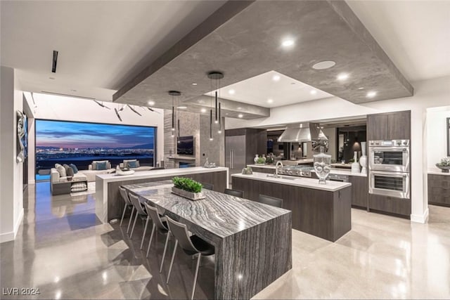 kitchen with a center island with sink, sink, dark brown cabinetry, decorative light fixtures, and stainless steel double oven