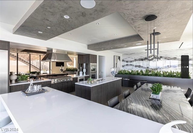 kitchen with a center island with sink, sink, appliances with stainless steel finishes, range hood, and a kitchen bar