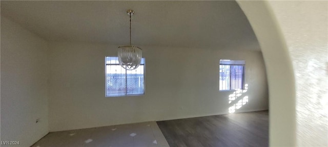 unfurnished room with plenty of natural light, hardwood / wood-style floors, lofted ceiling, and an inviting chandelier