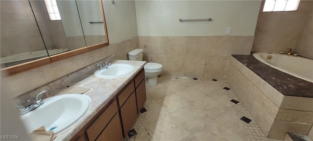 bathroom with a washtub, tile patterned flooring, toilet, vanity, and tile walls