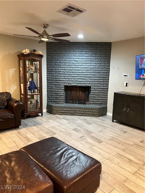 living room featuring a brick fireplace, ceiling fan, and light wood-type flooring