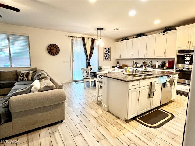 kitchen with white cabinets, decorative light fixtures, a healthy amount of sunlight, and an island with sink