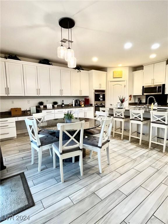 kitchen with stainless steel appliances, light hardwood / wood-style flooring, pendant lighting, a kitchen island with sink, and white cabinets