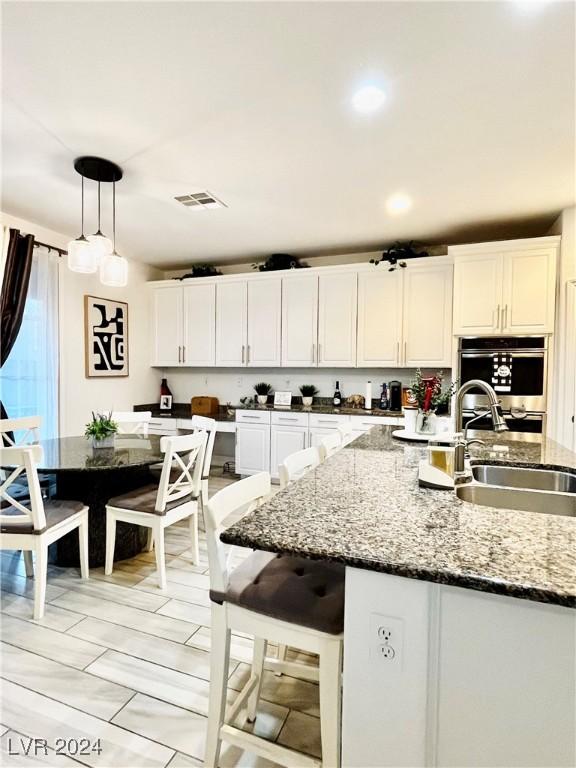 kitchen featuring white cabinets, sink, hanging light fixtures, and stone counters