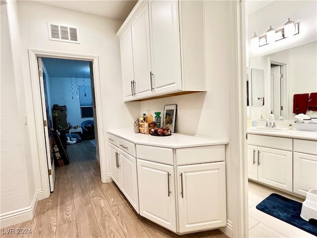 bar featuring light hardwood / wood-style floors, white cabinetry, and sink