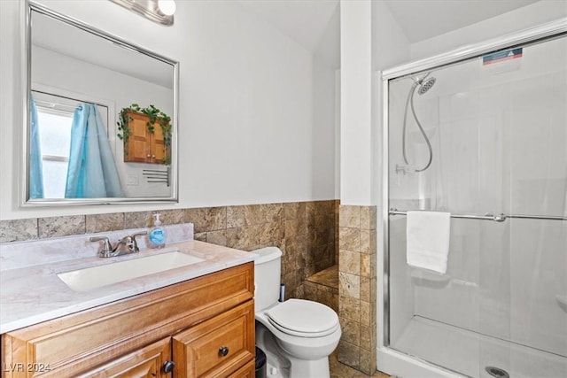 bathroom featuring vanity, toilet, a shower with door, and tile walls