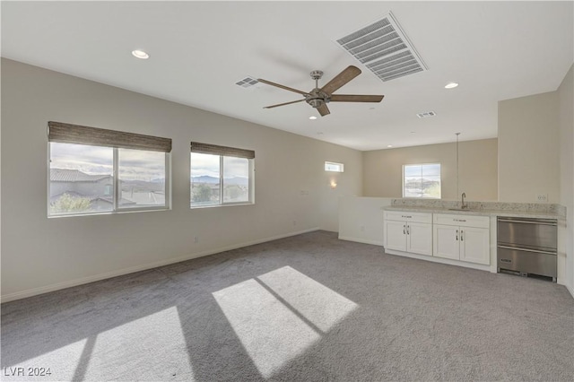 unfurnished living room with ceiling fan, sink, and light carpet