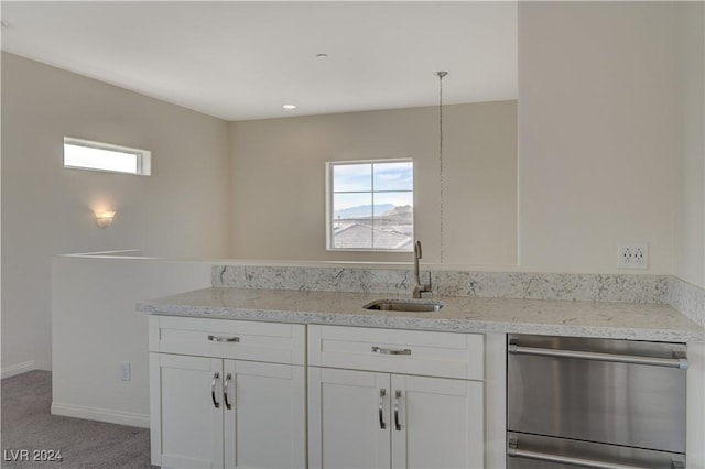 kitchen featuring light colored carpet, sink, dishwasher, white cabinetry, and hanging light fixtures